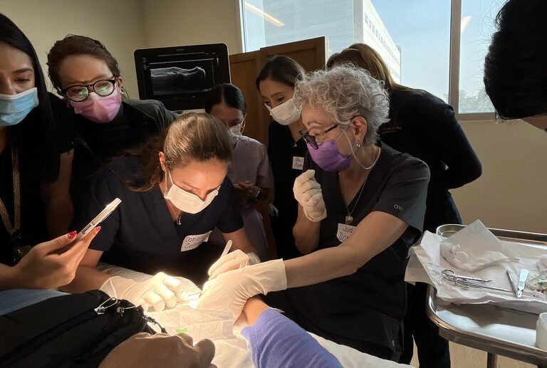 Several dermatologists observing a colleague perform surgery.