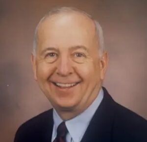 Photo of Dr. James Ertle in a dark blue suit, pale blue shirt and striped tie, against a muted background.