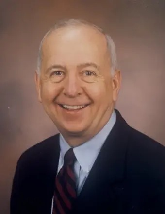 Photo of Dr. James Ertle in a dark blue suit, pale blue shirt and striped tie, against a muted background.