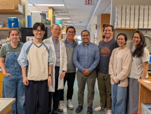 Five men and three women smiling at the camera, against the backdrop of a research lab.