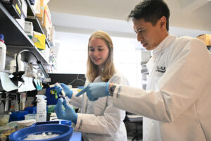 Woman in white lab coat with a man in white lab coat in laboratory setting.