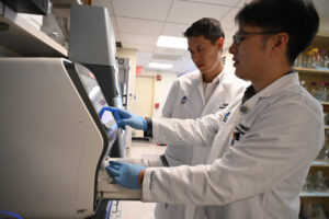 Two men in white lab coats standing before medical equipment, in laboratory setting.