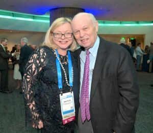 A woman dressed in black lace and a man with a dark suit and red tie smile at the camera during a social event.